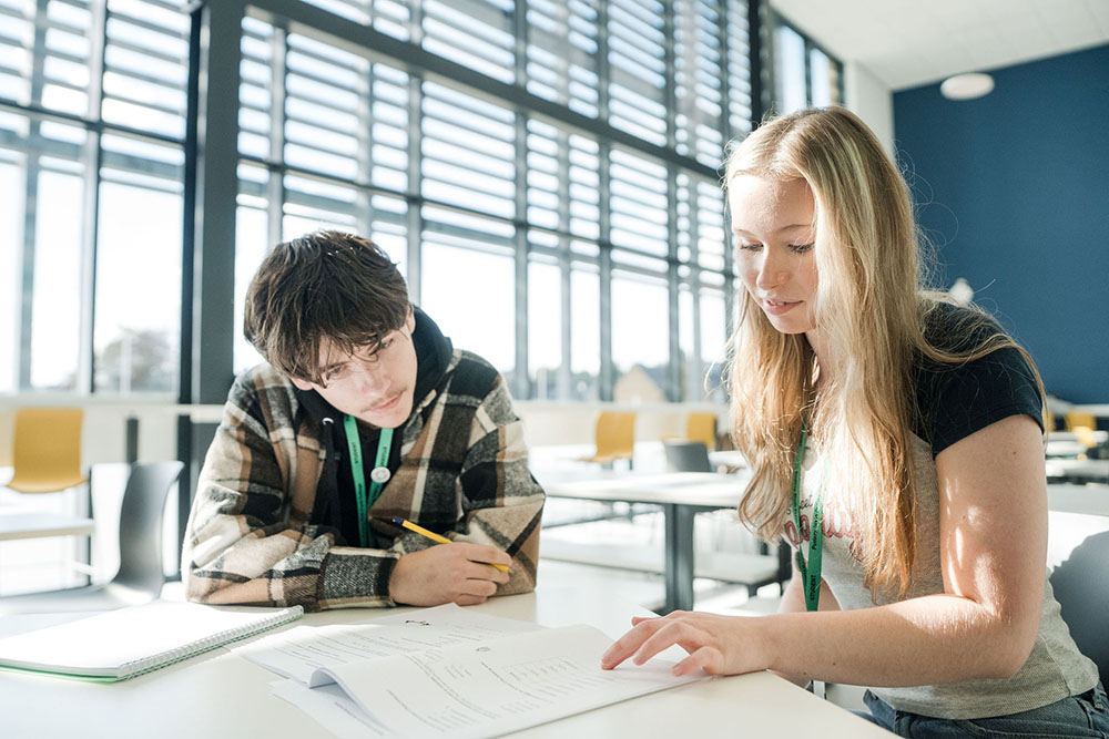 Two students sitting in classroom at a desk discussing work together