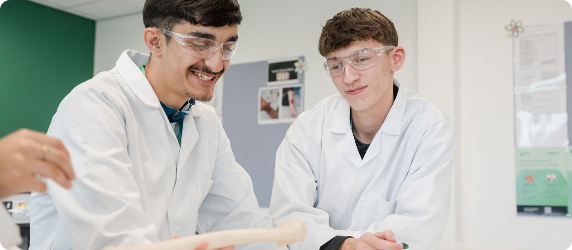 Students wearing white lab coat and safety goggles smiling looking at project