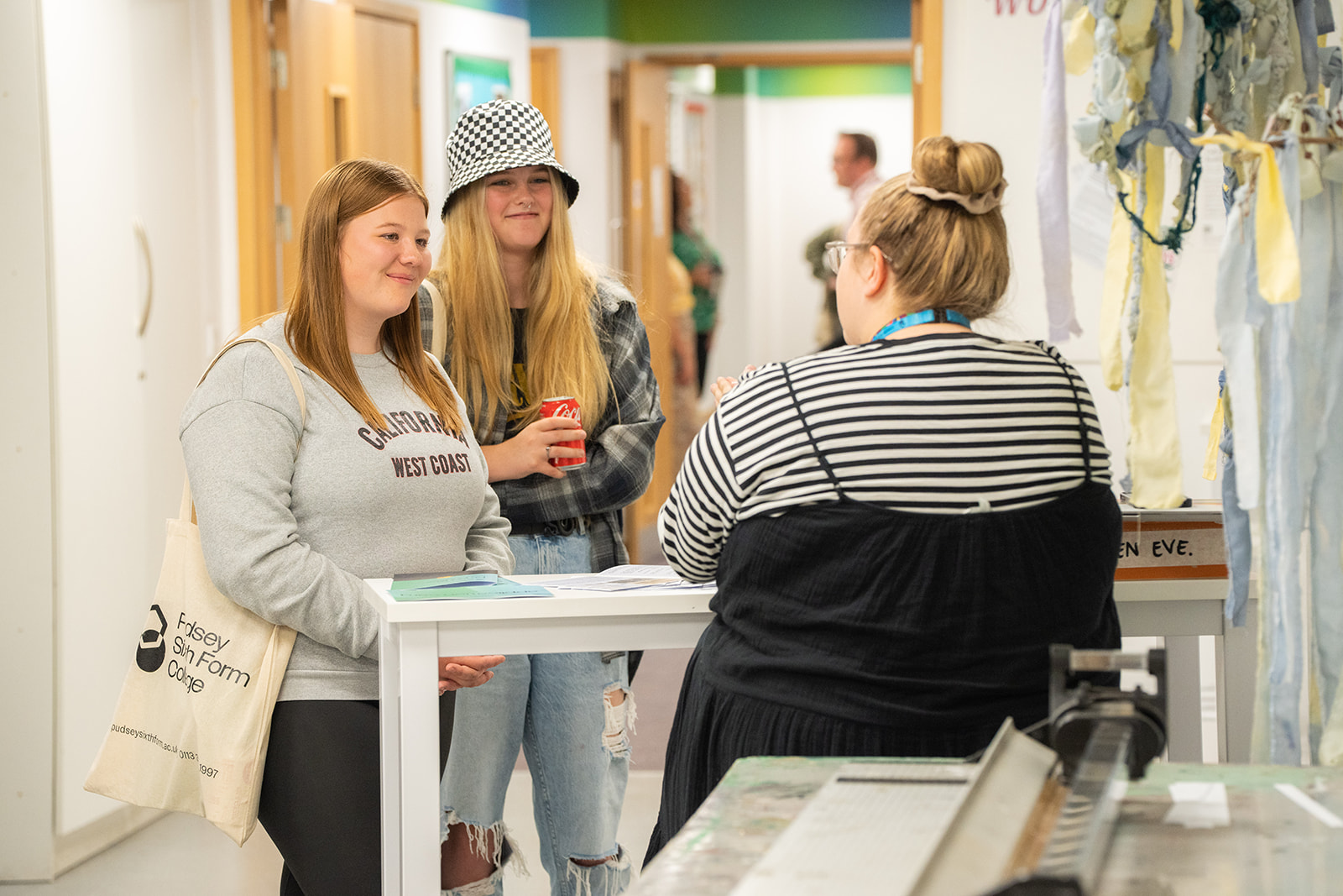 Two female students standing talking with course tutor in classroom