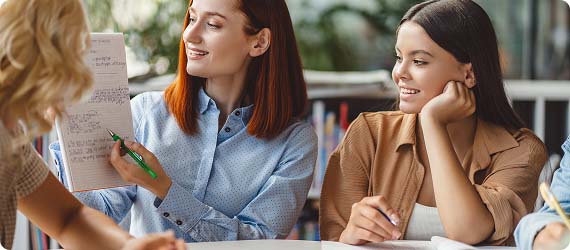 Students sat looking at work written in an exercise book held up by another student