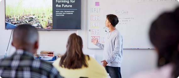 Student stood in front of class presenting whilst looking at information on a whiteboard