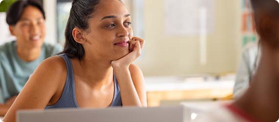 Student sat at desk in classroom with chin resting on hand looking thoughtful