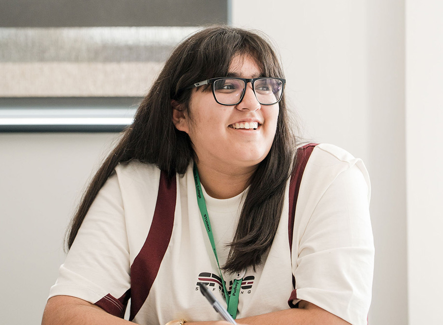 Student wearing glass sitting in classroom smiling