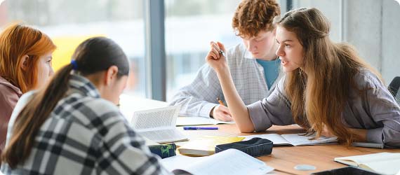 Four students sat in a classroom around a table with textbooks having a discussion