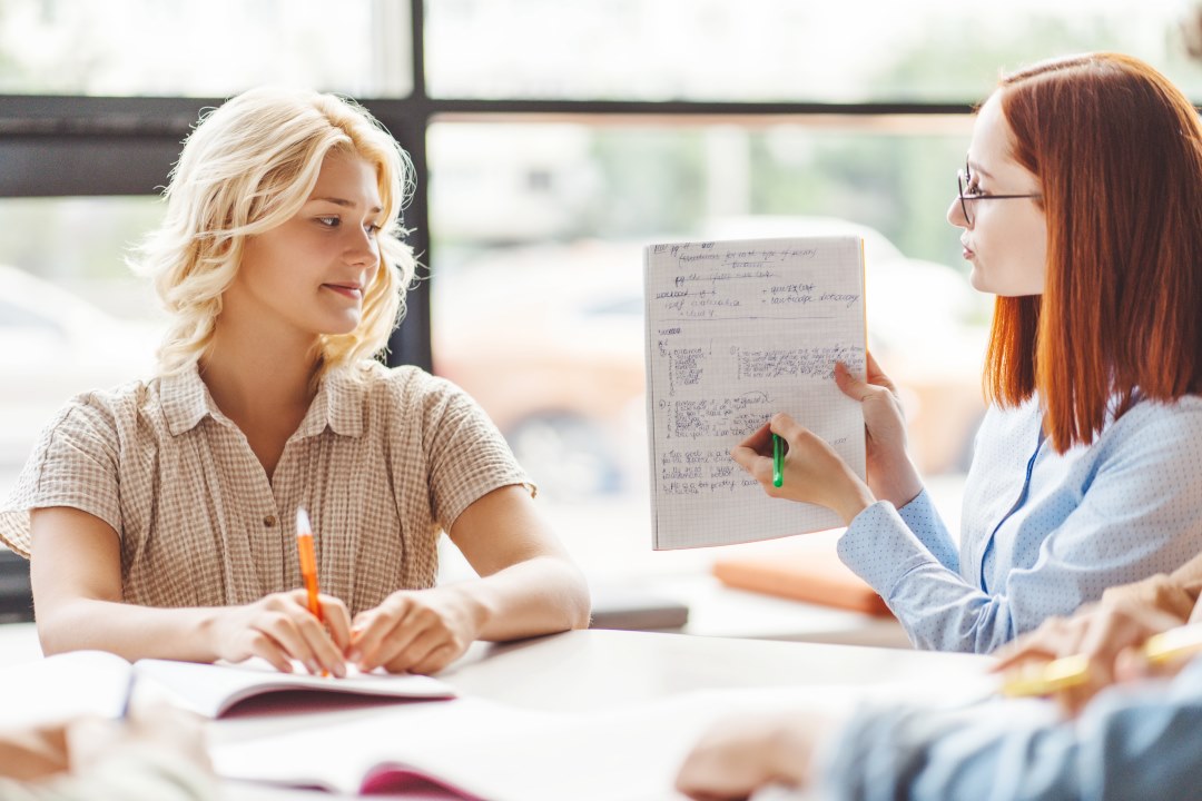 Two female students sat in a sunny classroom talking to one another