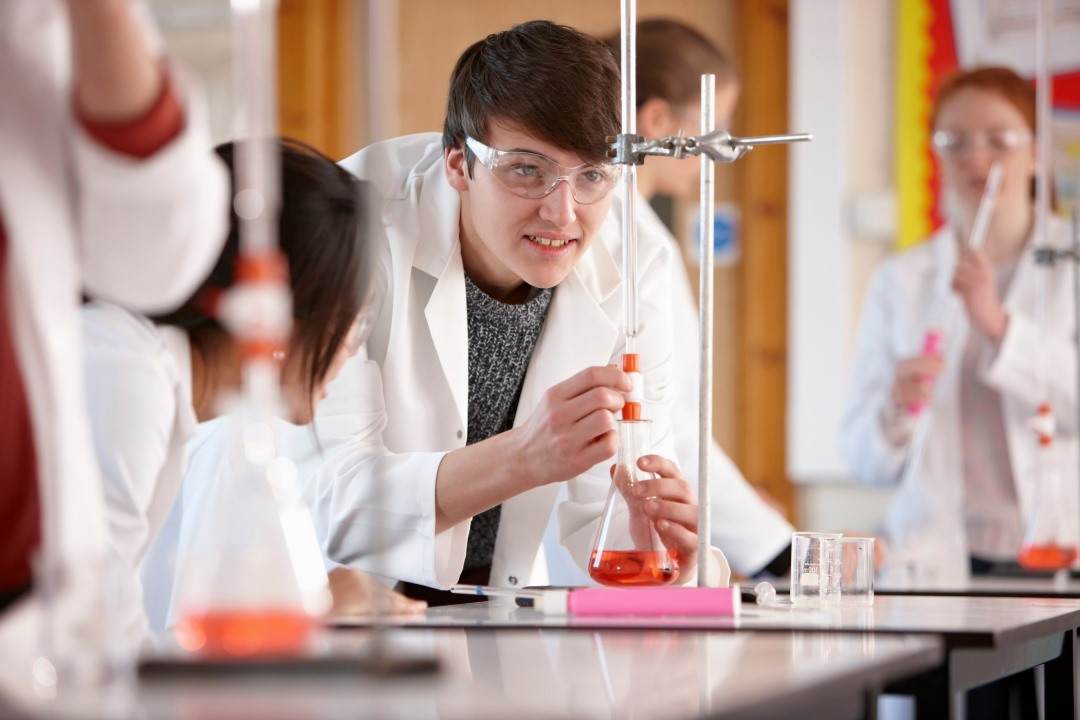 A student in a science lab wearing a lab coat conducting an experiment with chemicals