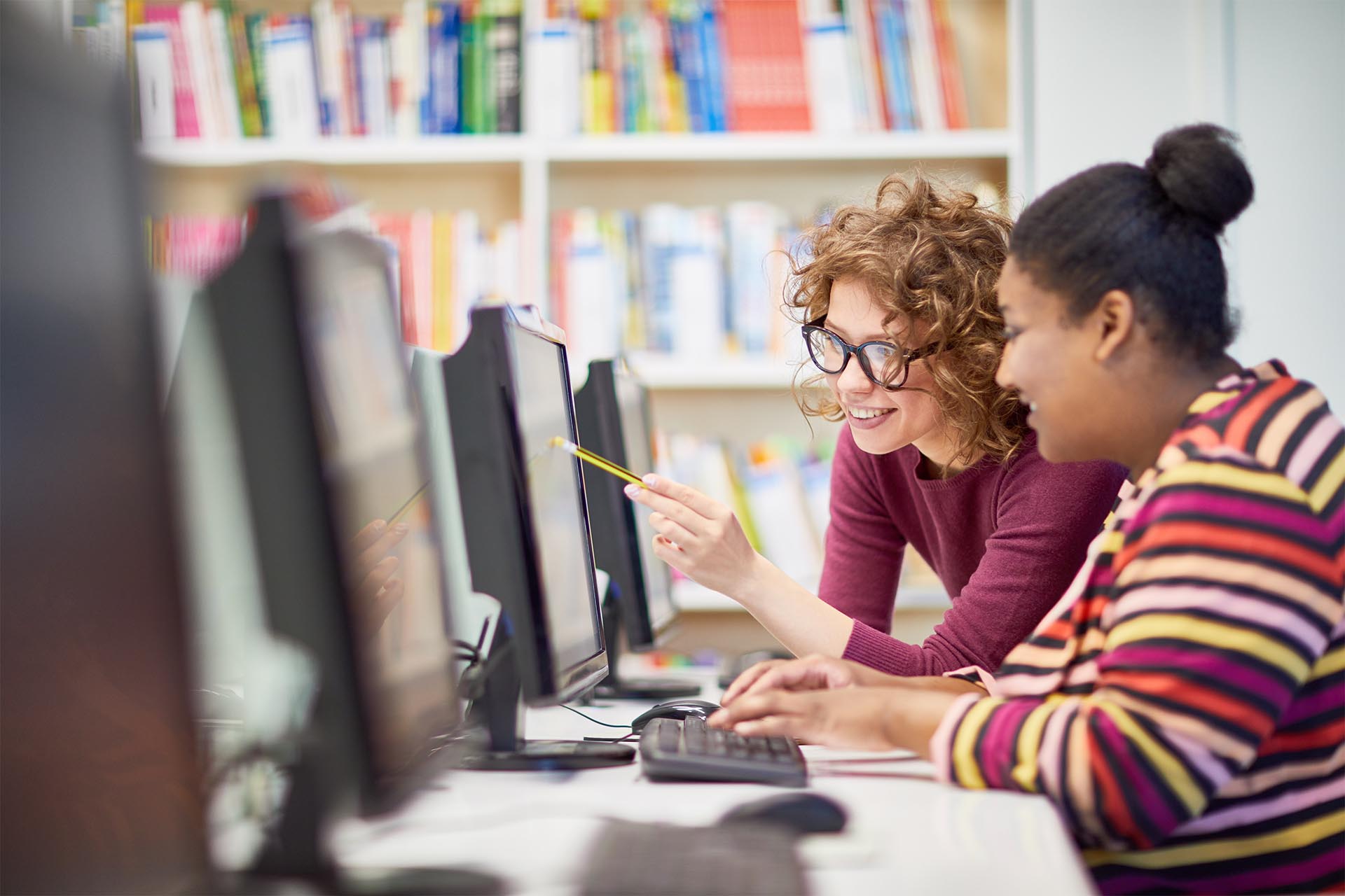 Two tutors having discussion in front of desktop computer in the library