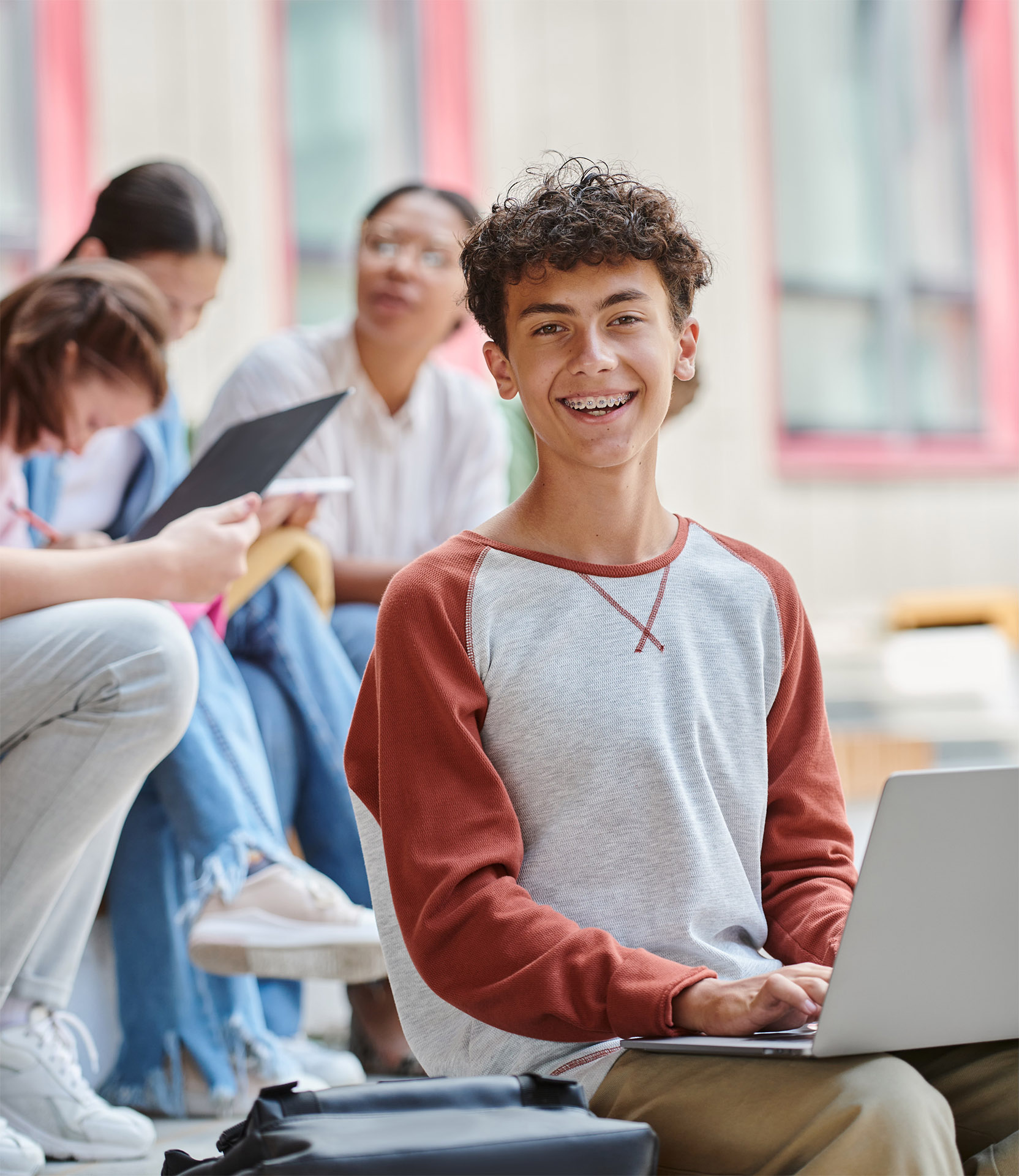 Student in raglan shirt smiling with a few students sitting at the back