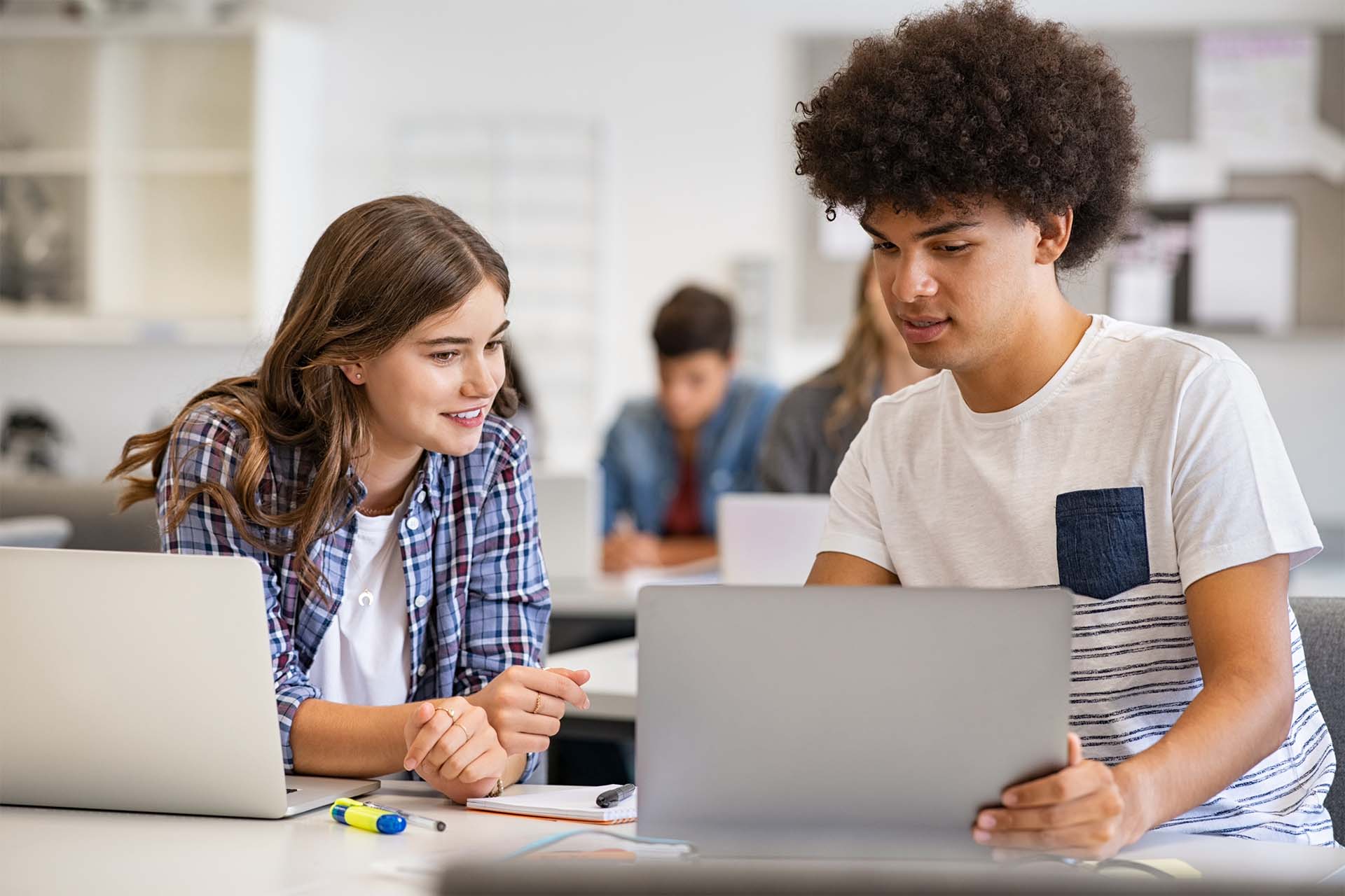 Class of students talk among each other in front of their laptops