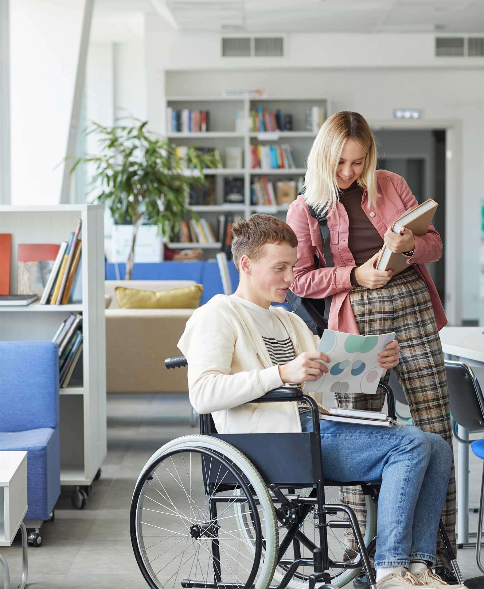 Female student standing talking to student in wheel chair in the library