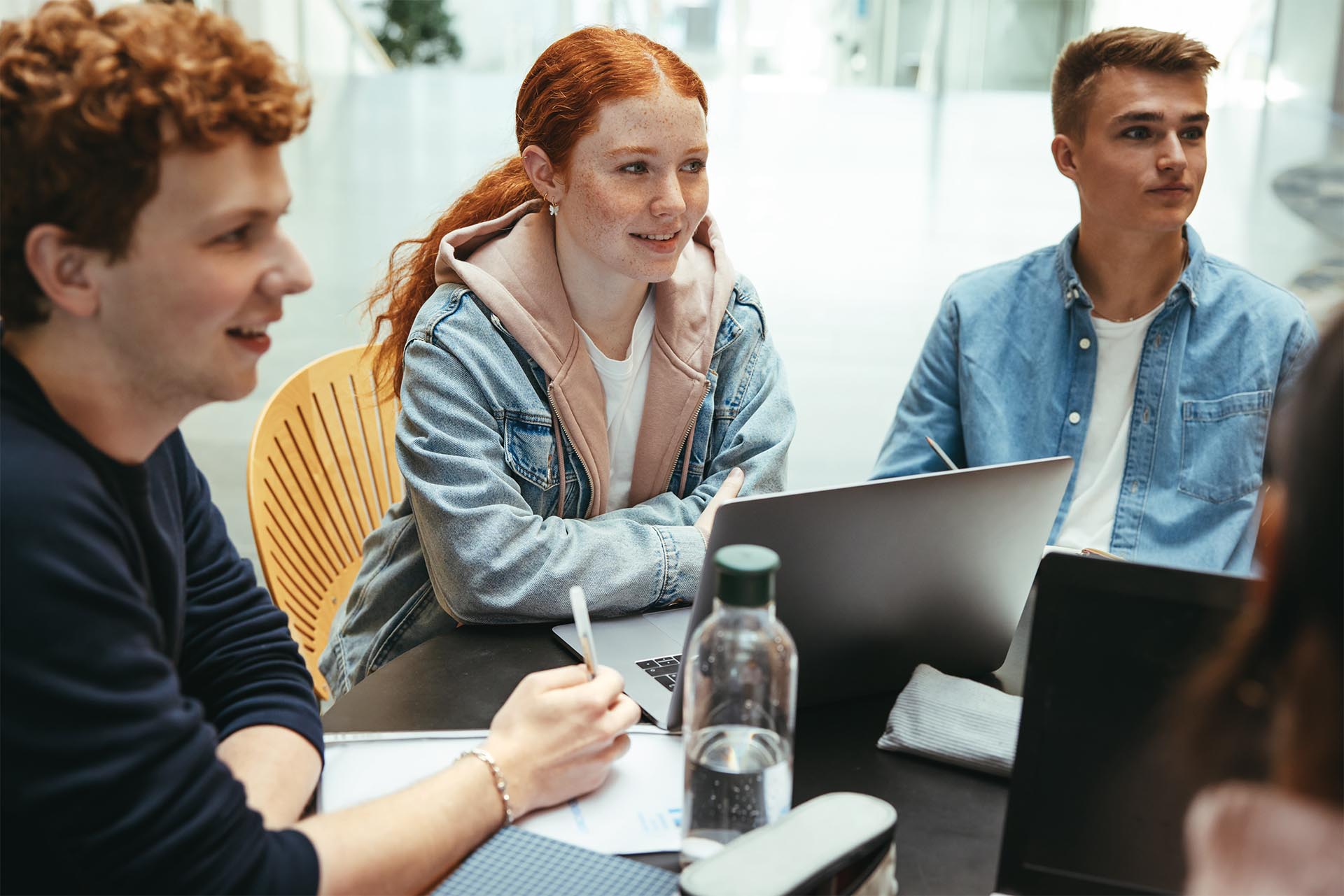 Students smiling having discussion with laptop, water bottle and notes on the table