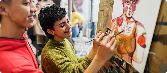 Two students painting on canvas together and smiling in art studio