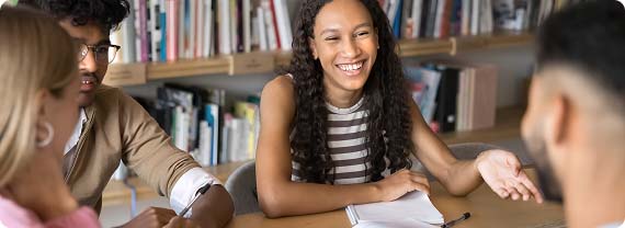 Students sat around a table in the library smiling and chatting