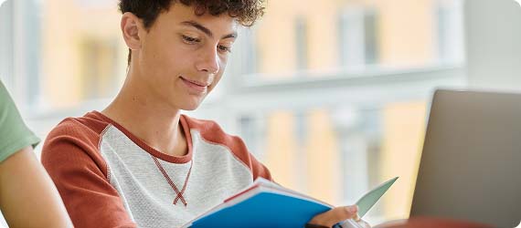 Student looking down thoughtfully reading a book with large windows behind