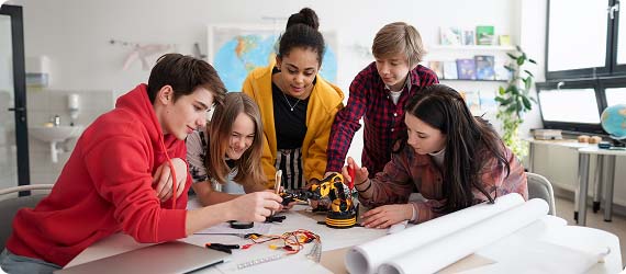 Group of five students in a classroom building an electrical circuit together