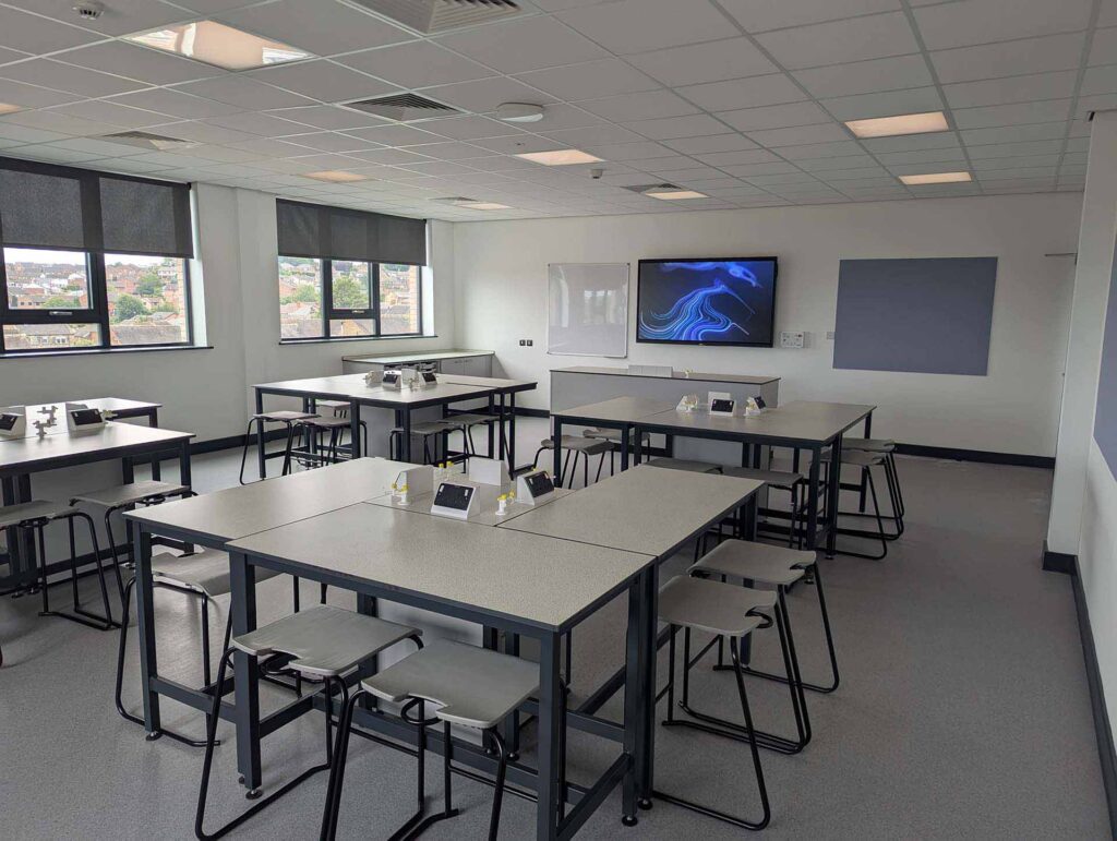 Pudsey Sixth Form College classroom with grey tables and stools, with big screen TV hanging at the front