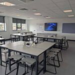 Pudsey Sixth Form College classroom with grey tables and stools, with big screen TV hanging at the front