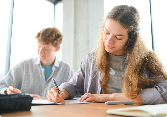Two students sat at a desk in a classroom writing notes