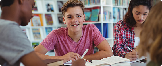 Students sat studying in library with one student looking towards the camera and smiling