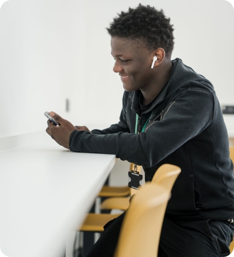 Student wearing earphone sitting down looking at his phone smiling