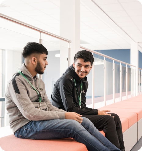 Two students sitting down on pink seat having conversation