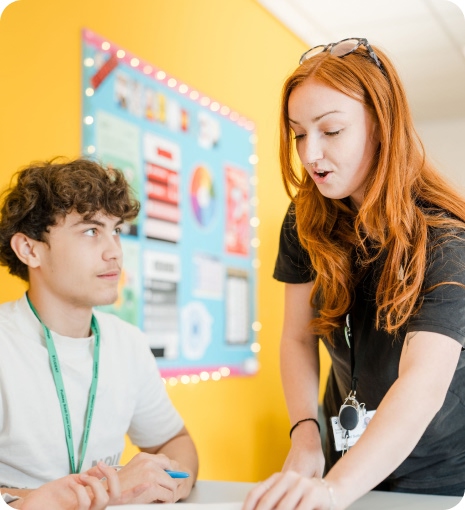 Tutor standing talking to student sitting down in classroom
