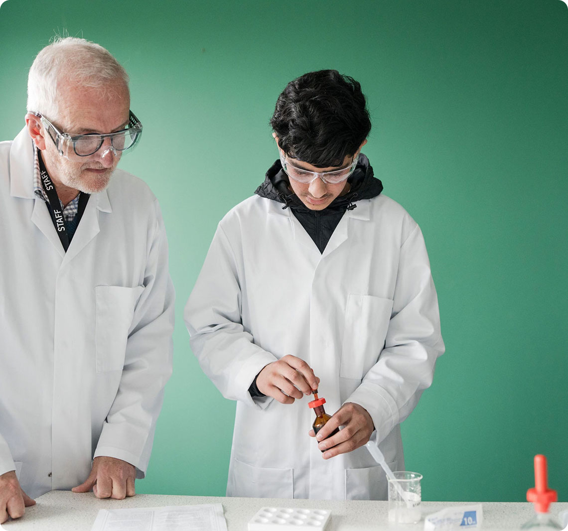 Tutor and student wearing white lab coat standing analysing samples