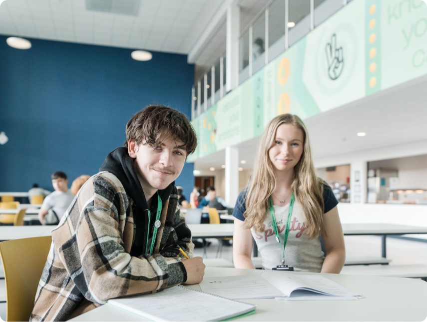Two students sat in the canteen with notes on the table smiling