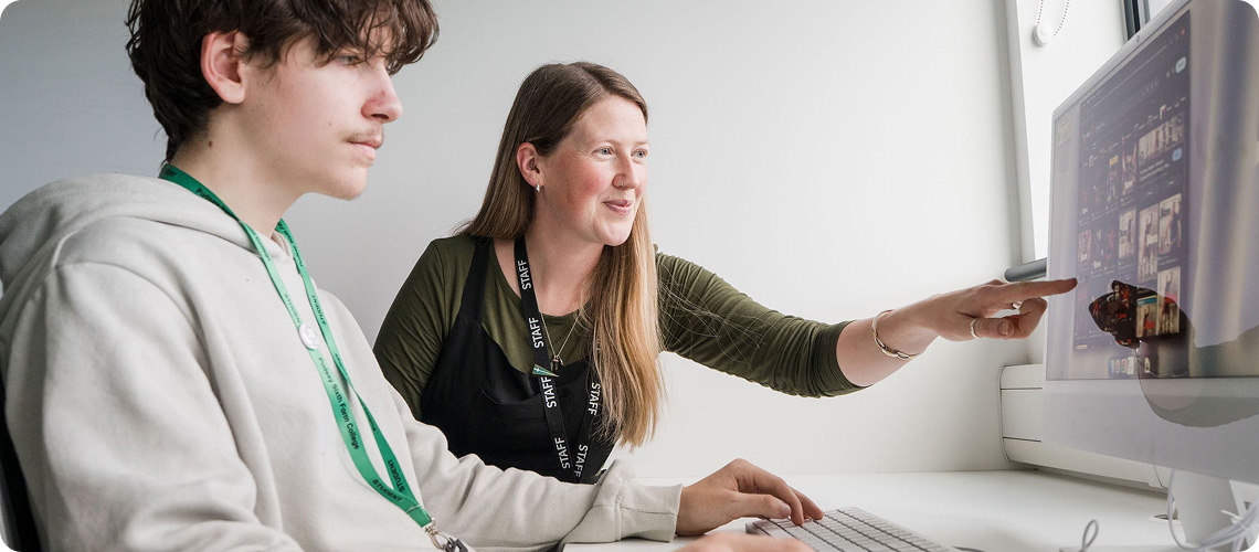 Tutor talking to student in classroom pointing at computer monitor
