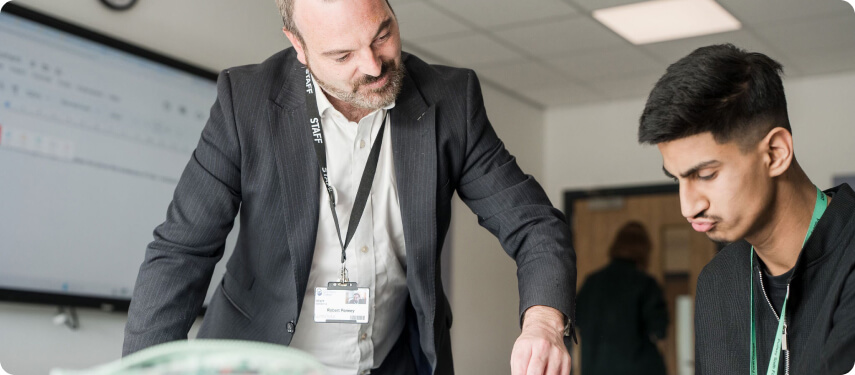 Tutor standing talking to student who is sitting down in classroom