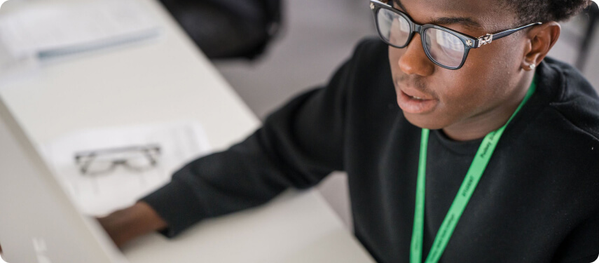 Student in black top wearing glass sitting down in the classroom working in front of computer