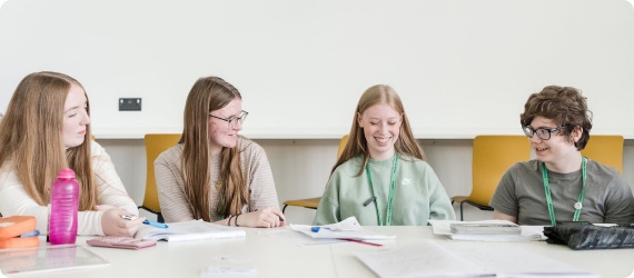 Four students sitting down having discussion with pens and notes on the table