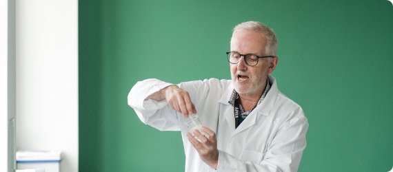Tutor wearing white lab coat standing analysing samples