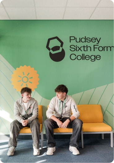 Two students sitting by green graphic wall with Pudsey Sixth Form College sign and logo, on yellow chair in waiting area talking