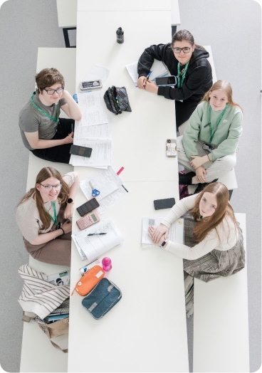 Students sitting in canteen with notes and stationery on the table looking up