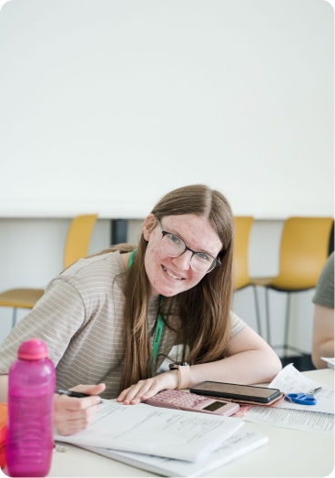 Student sitting down writing notes with phone and pink water bottle on the table