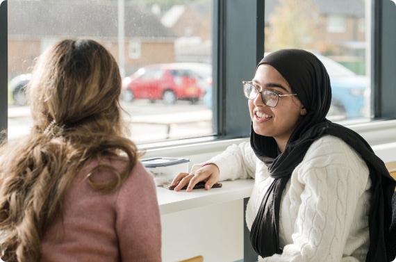Two students sitting down by the window having conversation