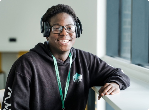 Student in black top wearing headphone sitting next to window smiling
