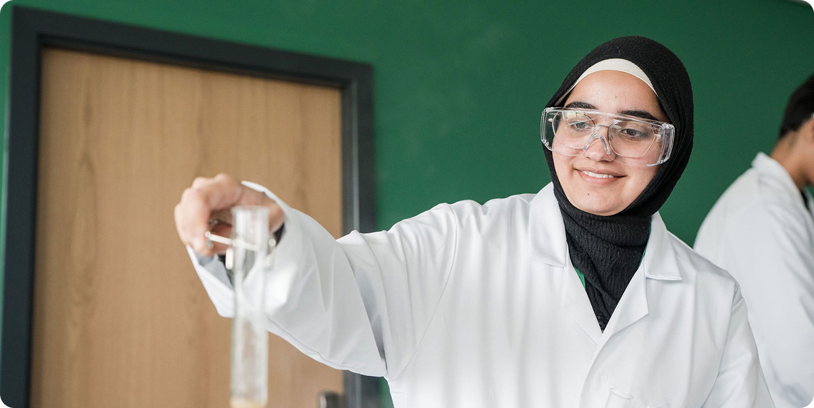 Student wearing white lab coat and safety goggle conducting experiments