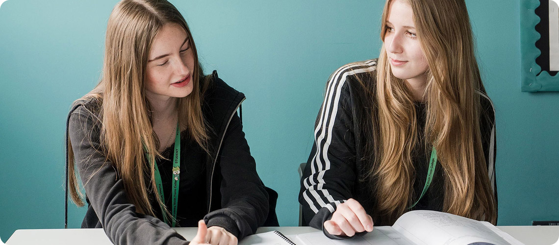 Two female students wearing green lanyard having discussion in classroom