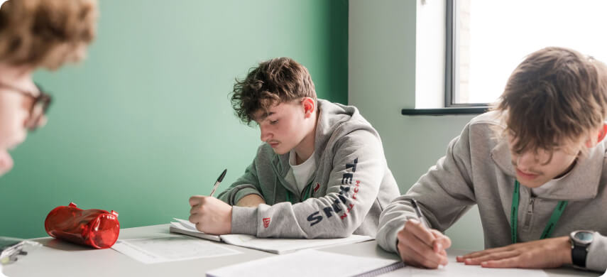 Students sitting in classroom writing notes on table