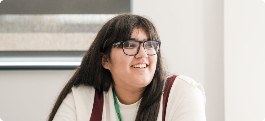 Student wearing glass sitting in classroom smiling
