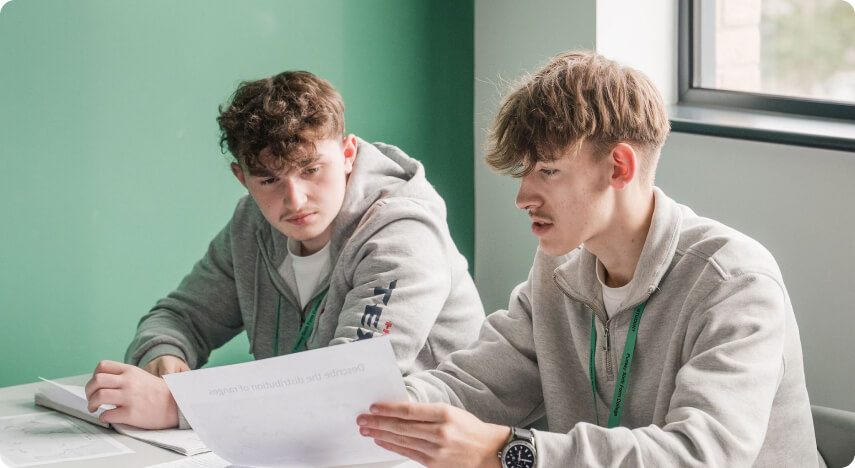 Students sitting down with one student holding a piece of paper having discussion in classroom