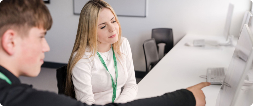 Students wearing green lanyard sitting down in the classroom with one student pointing to the monitor screen