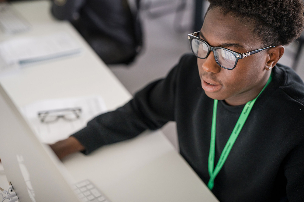 Student in black top wearing glass sitting down in the classroom working in front of computer